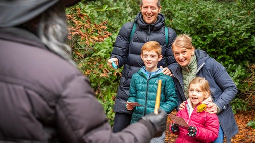 A family smile at a volunteer dressed in black, waving a wand and wearing a witch's hat.